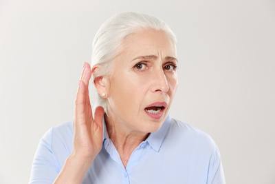 Close-up  of charming elderly woman, holding hand by her ear and struggling to hear something, isolated on white background